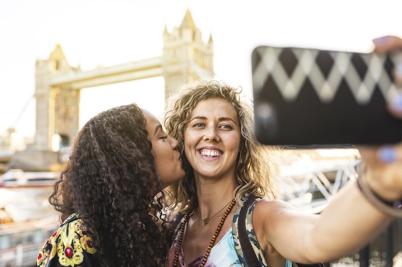 same sex couple taking a selfie with the London Bridge tower in the background