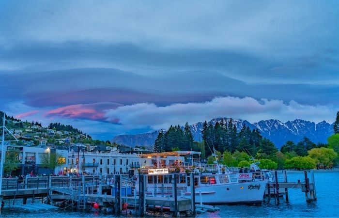 White midsized boat docked on a port with dwellings on a mountain behind it