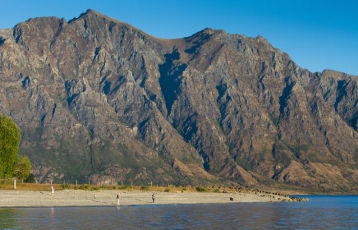 Two people standing on the shore with a rocky mountain behind them