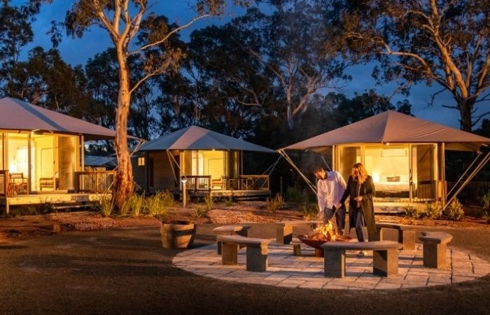 couple near fire with safari tents behind them