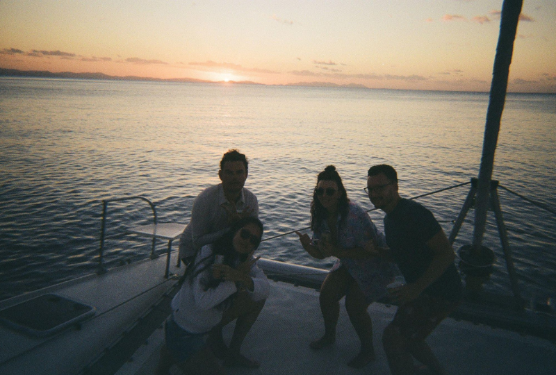 a group of friends having their picture taken on the boat deck while sailing around Whitsunday Island