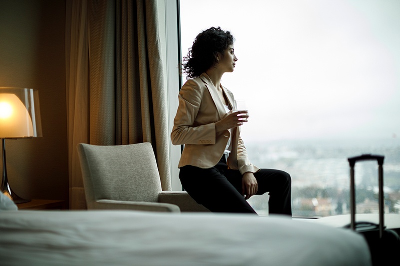 Woman sits in hotel room and looks out window