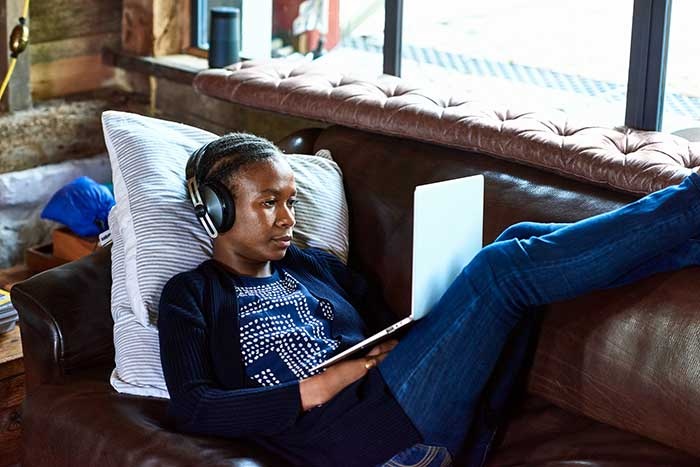 Woman laying on the coach with headphones and laptop