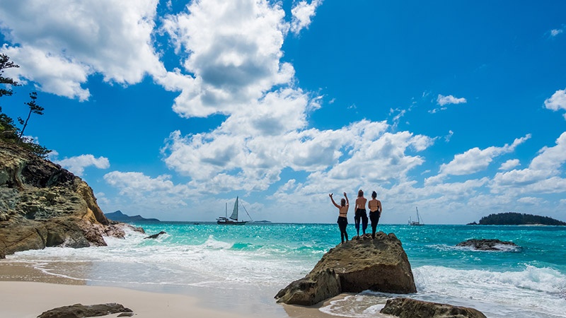 three tourists standing on a big rock enjoying the ocean