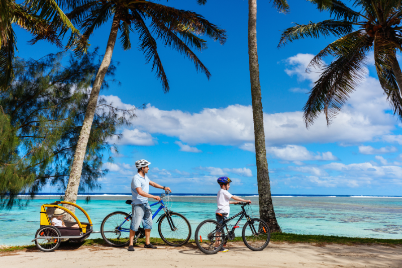 Father and kids enjoy a bike ride alongside the beautiful beaches of Rarotonga 