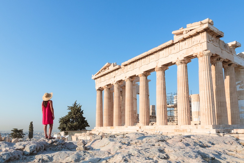 A woman in a red dress looks at The Acropolis, Athens.