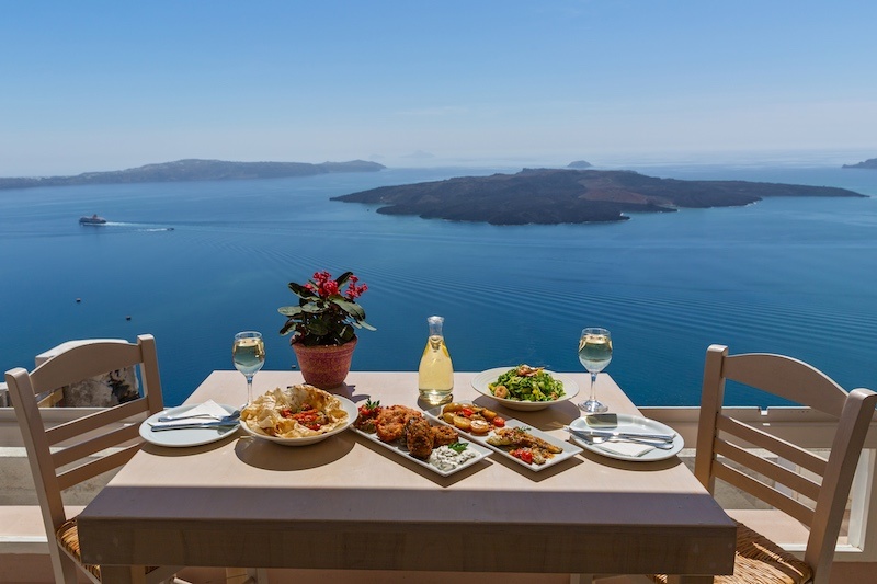 Lunch overlooking a blue sea and distant islands in Santorini, Greece.
