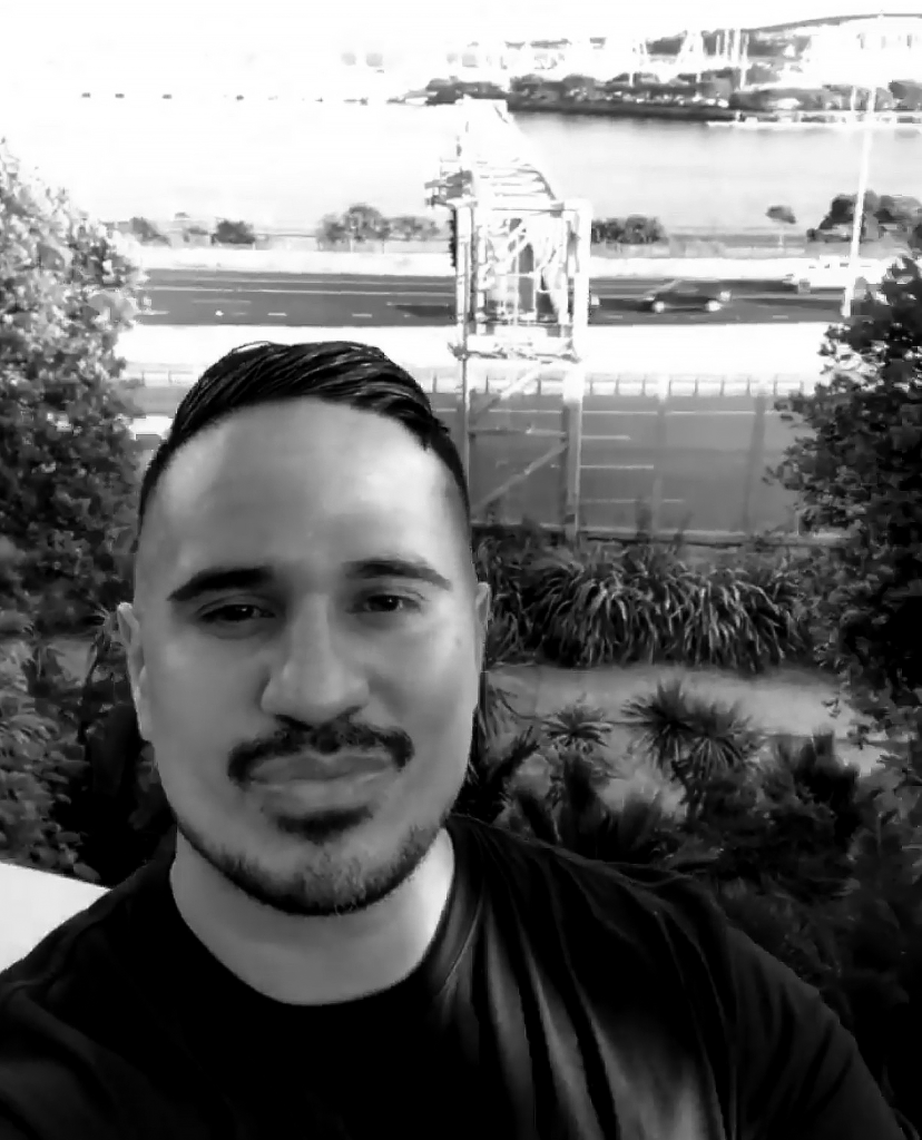 A balck-and-white close-up of a bearded Maori man with an Auckland motorway in the background