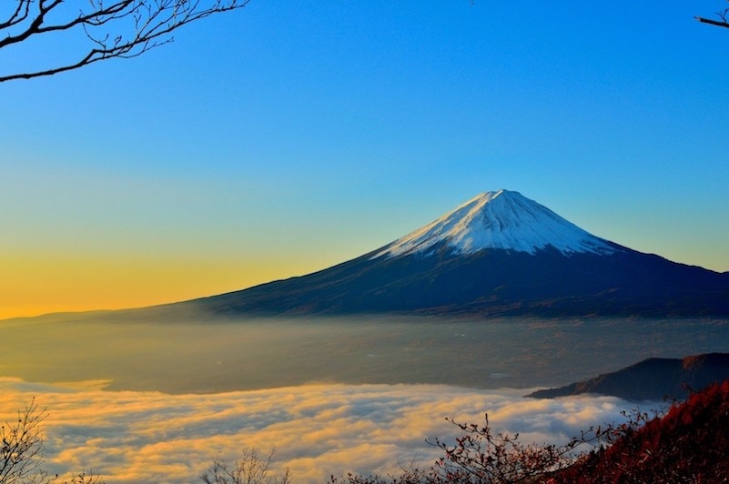 Mist surrounds the foot of Mt Fuji at sunrise below a blue and orange sky.