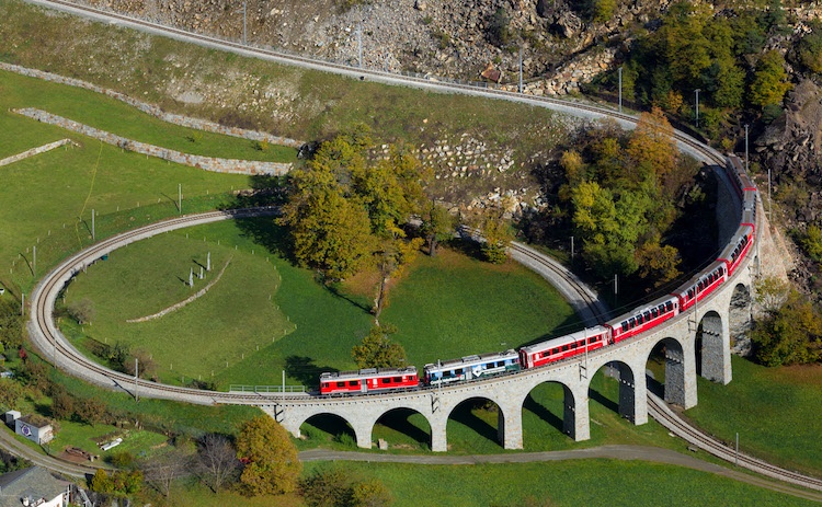 A passenger train descends a spectacular spiralling bridge with many archway supports in Switzerland.