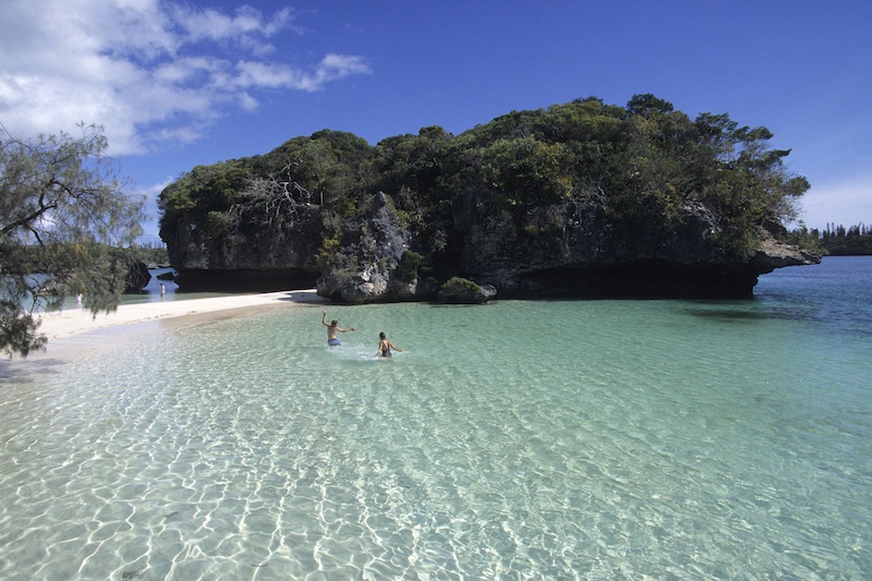A couple swims in the clear waters of Kanumera Bay in the Isle of Pines, New Caledonia.