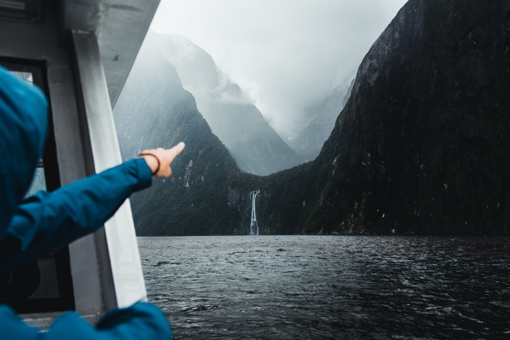 Person pointing towards the mountains with water falls