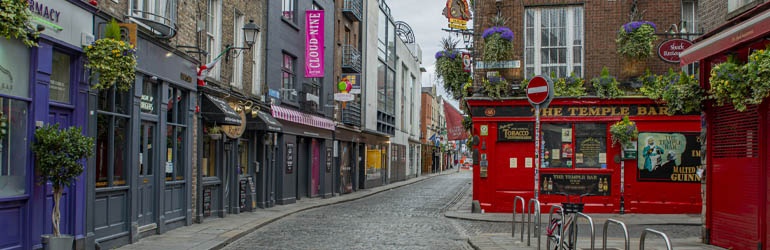 A cobbled street in Dublin where the iconic red facade  of The Temple Bar is situated on the corner.