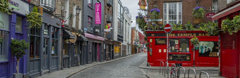 A cobbled street in Dublin where the iconic red facade of The Temple Bar is situated on the corner.