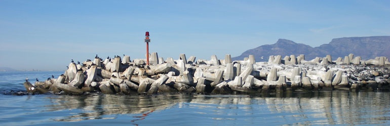 The signal light on the concrete block pier at the edge of Robben Island, Cape Town, South Africa with Table Mountain in the Background