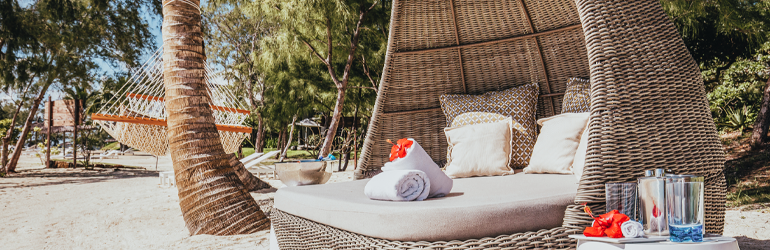 A large outdoor lounge chair on a beach by a hammock and a palm tree