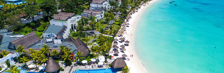 A drone's view of a resort by a white sandy beach and azure lagoon