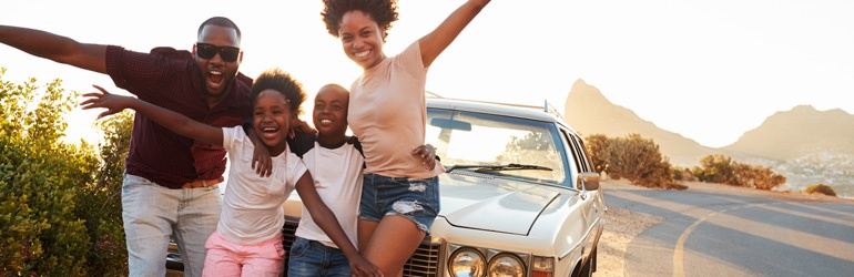 A happy family taking a photo in front of a car that is parked next to the road