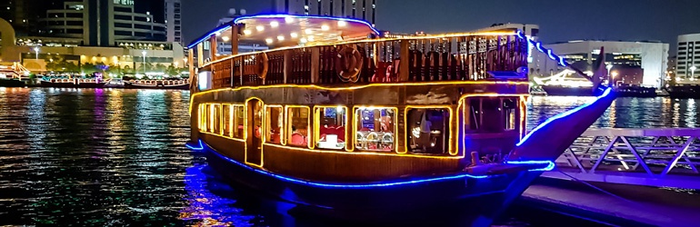 A restaurant river cruise ship lined with colourful neon lighting at night.