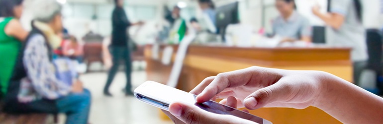 A women's hands scroll over a touch screen with a bustling shop in the background