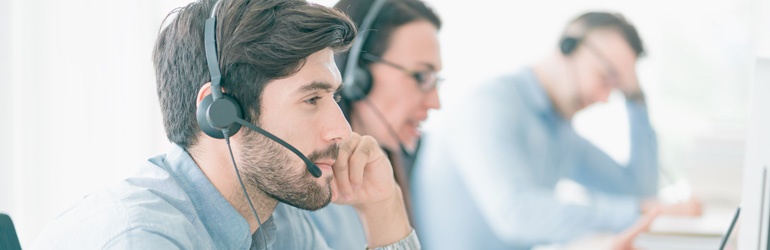 A man with a headset works with colleagues in a call centre