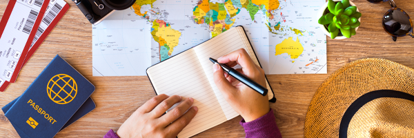 A person writing in a journal with a map and passport on the table