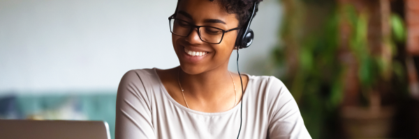 A smiling lady wearing headphone working on a laptop