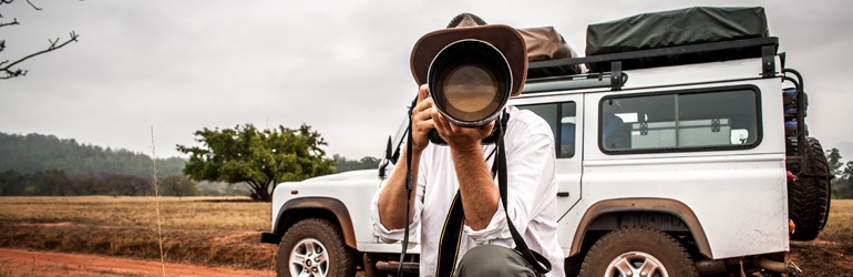 A person standing next to a white safari Jeep, using a camera to take a photo