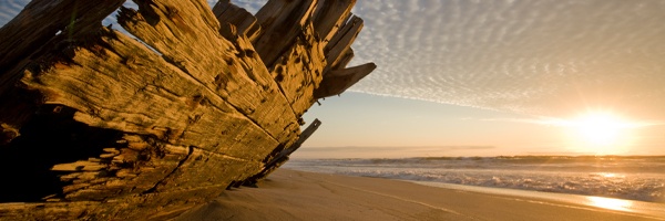 A wooden ship wreck on a beach with the sun setting