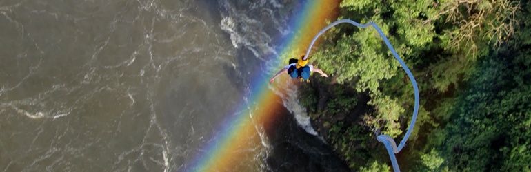 Looking down at a bungee jumper plummeting down towards a swift river and a misty rainbow