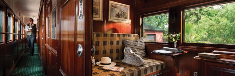 The wooden interior of a traditional passenger carriage with a waiter approaching an open cabin door