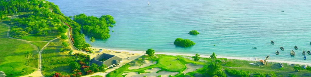 A drone's view of a beach-side golf course and boats moored near the shore