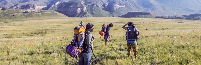 A group of people hiking through a field with mountains in the background