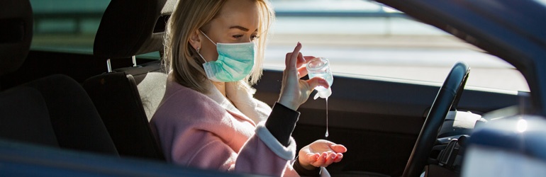A person in a car wearing a mask and using hand sanitiser