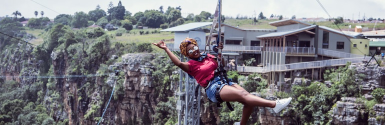 A woman waves while sitting in a harness suspended over a deep canyon