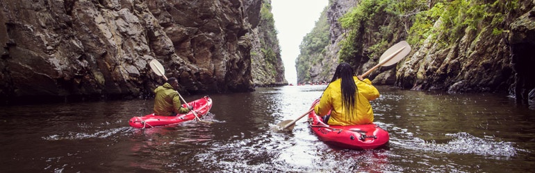 Two people in kayaks paddle through a narrow rocky canyon
