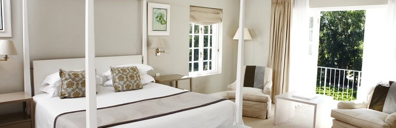 A large double bed with posts in a motel room with French doors leading to trees