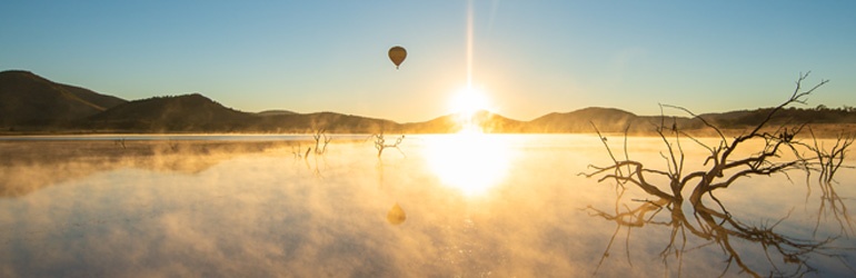Sun rising over a lake with mist and  a hot air balloon