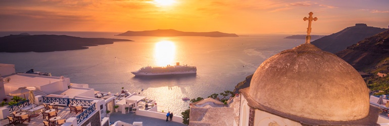 A cruise ship sails to shore in a bay below Santorini, Greece at sunset