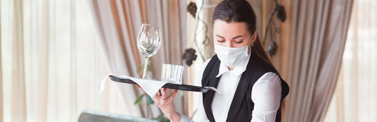 Female waitress dressed in black and white wearing a mask holding a tray