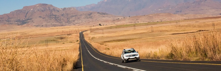 White car driving on a desolated road with brown surroundings 