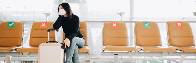 Woman wearing a mask and sitting alone at the airport with social distancing markings on the seat