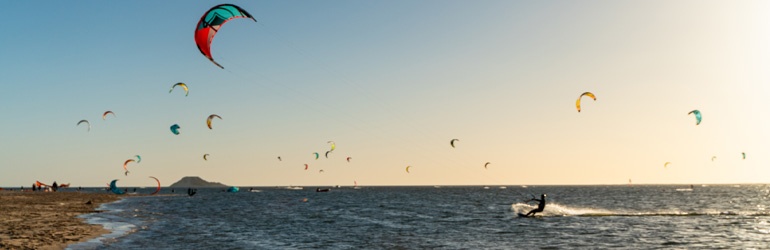 Kite-surfers' sails fill the sunset sky by the beach