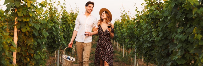 A couple walking through a vineyard with a picnic basket